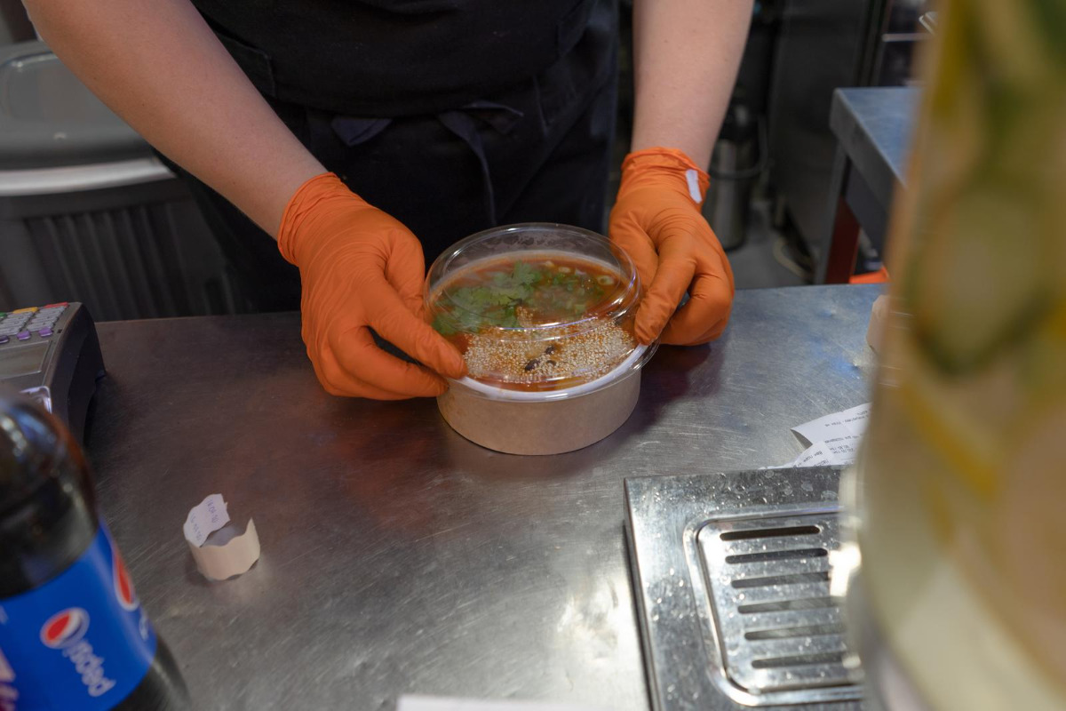 Fast food worker prepping soup in a paper bowl.