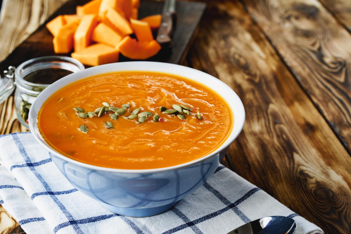 Creamy pumpkin soup with pumpkin slices on a wooden table.