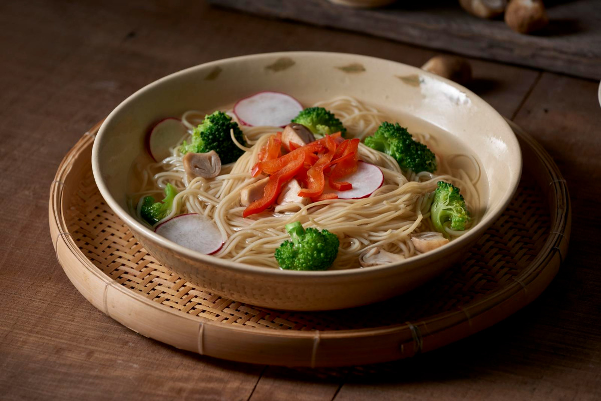 A bowl of vegetable soup with noodles in a wooden basket.