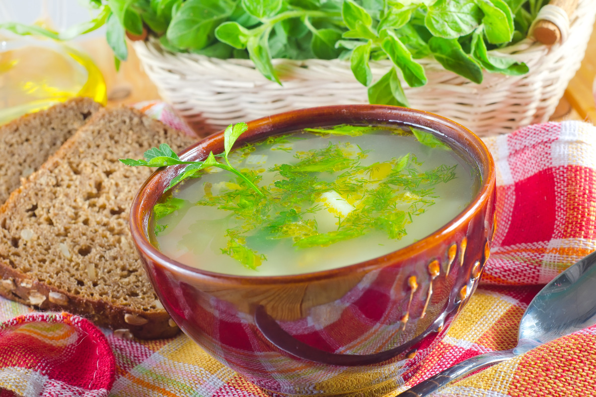 A bowl of vegetable clear soup with a side of bread.