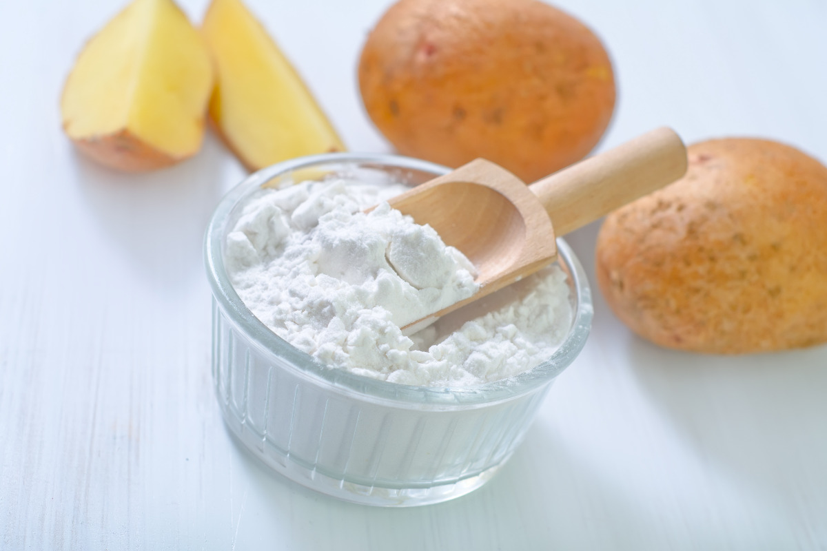 A bowl of potato starch with potatoes in the background. 