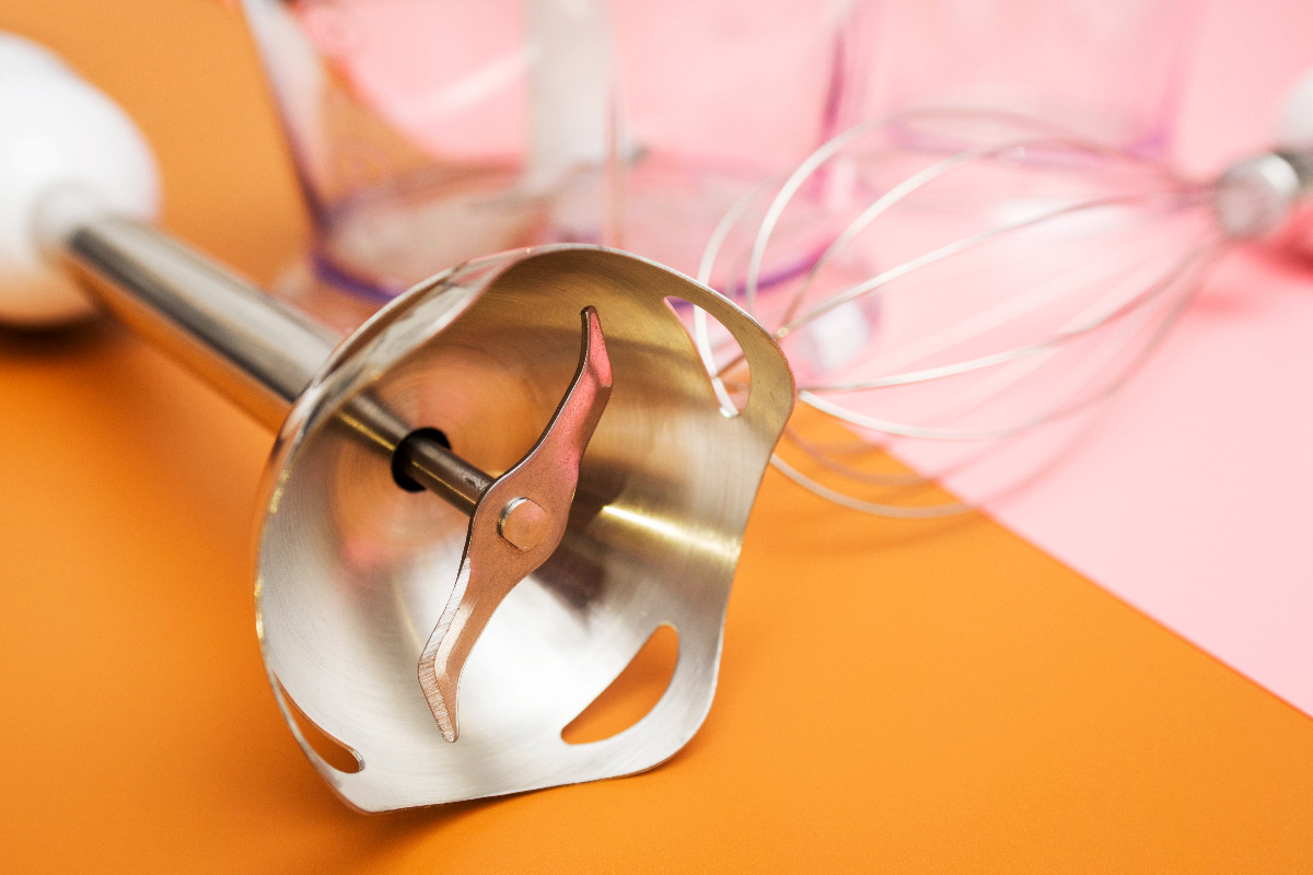 A soup immersion blender next to a whisk.