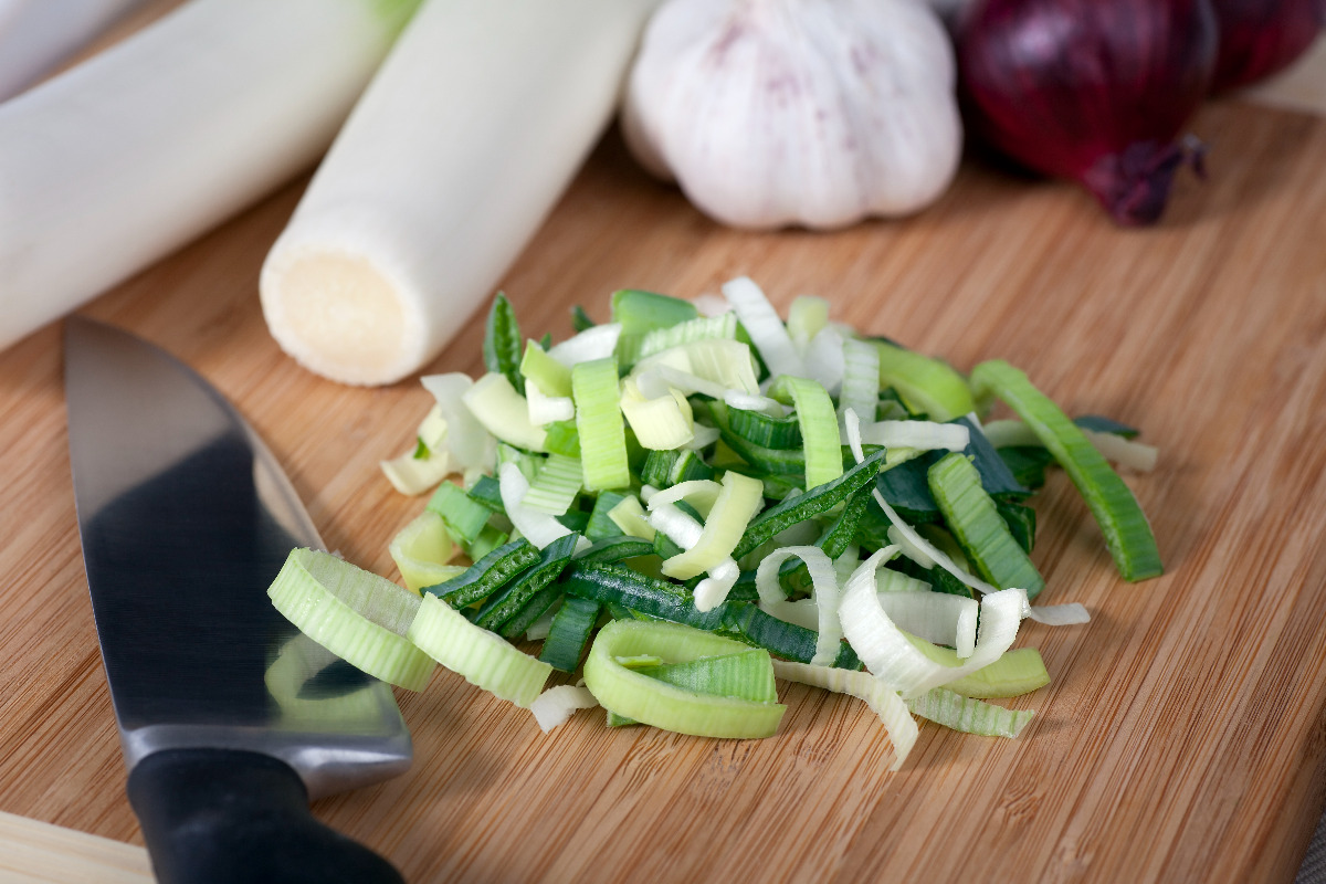 Chopped leaks next to a knife and soup ingredients. 